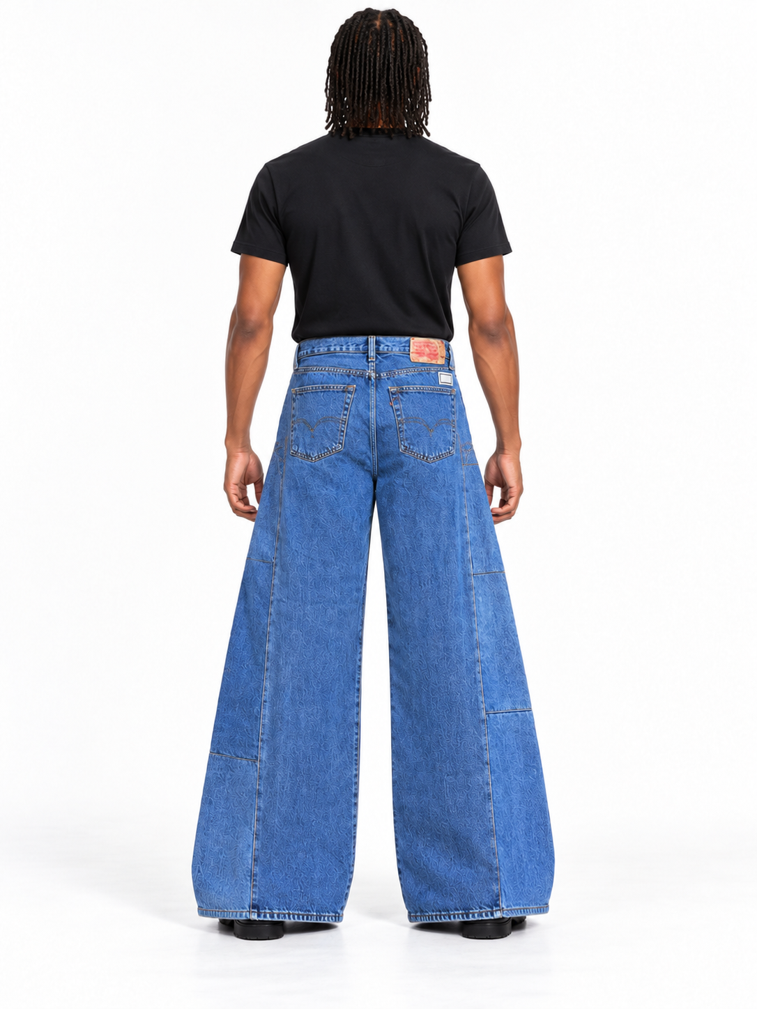 A model shown from the back wearing a pair of wide-leg blue denim jeans with a black t-shirt, photographed against a solid white studio background.