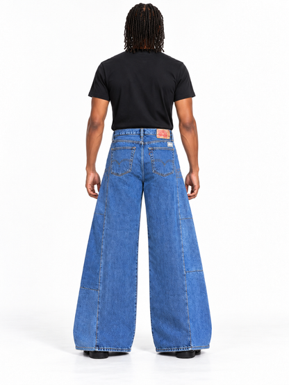A model shown from the back wearing a pair of wide-leg blue denim jeans with a black t-shirt, photographed against a solid white studio background.