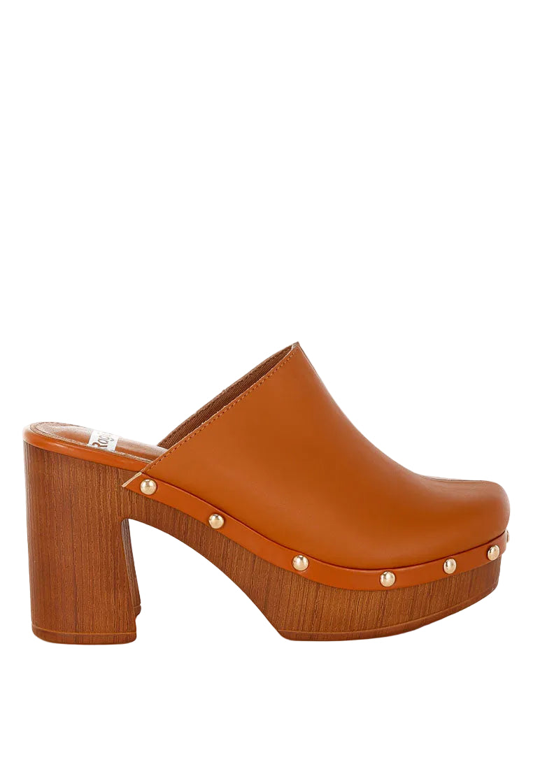 A single women's clog-style mule shoe in warm cognac brown faux leather, featuring a chunky wood-textured block heel, platform sole, and decorative gold-tone studs along the side, shown against a plain light gray background.