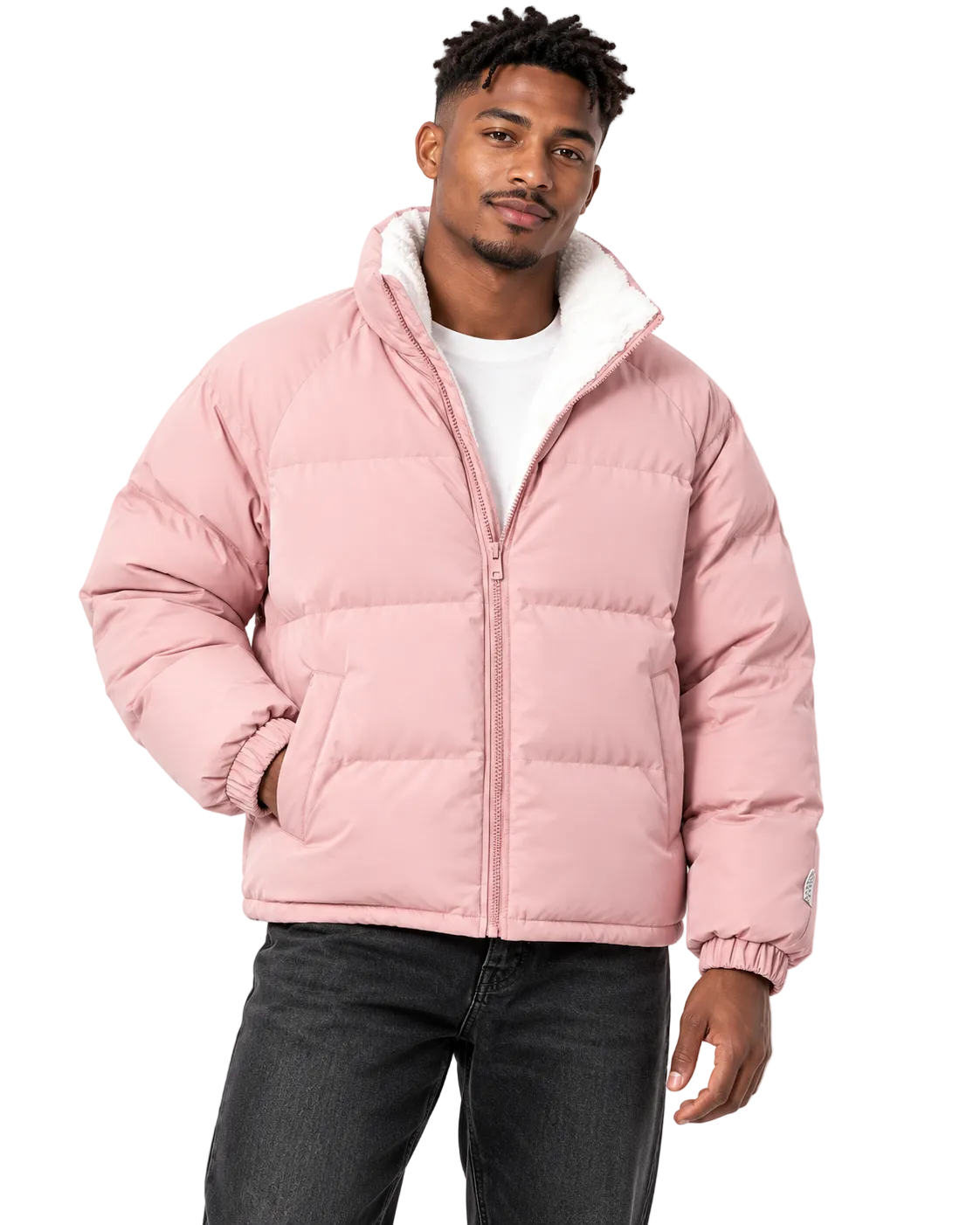 A man wearing a light pink puffer jacket with a white sherpa-lined hood, styled over a white t-shirt and dark gray jeans, against a plain white background.