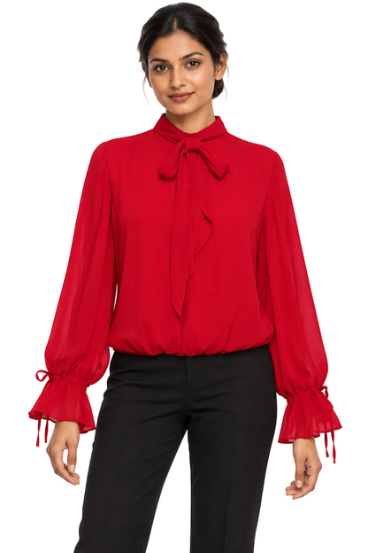 A woman wearing a bright red long-sleeve blouse with a high neck, bow tie detail at the collar, and ruffled tie cuffs, paired with black pants, against a plain white background.
