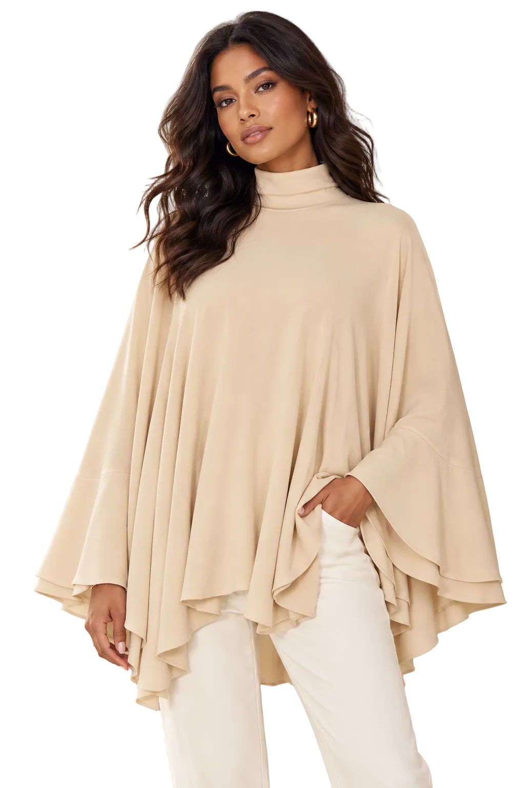 A woman modeling a beige high-neck, long-sleeve top with dramatic layered bell sleeves and an asymmetrical draped hem, paired with white pants in a softly lit architectural setting.