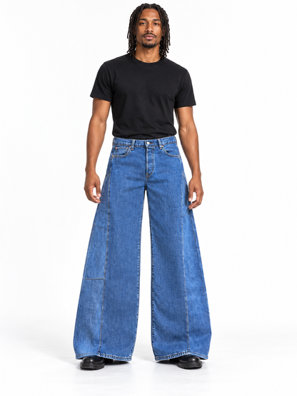 A man modeling a pair of wide-leg blue denim jeans with a black t-shirt, standing against a plain white studio background.