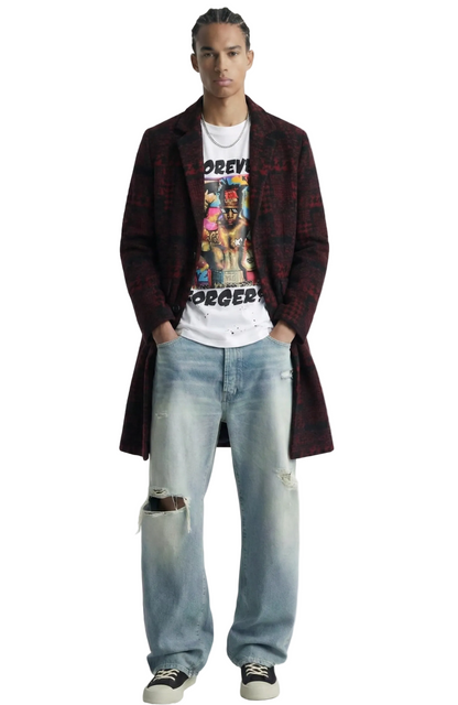 A model stands against a white background wearing a long dark red and black plaid coat over a white graphic t-shirt, light-wash distressed jeans, and black low-top sneakers.
