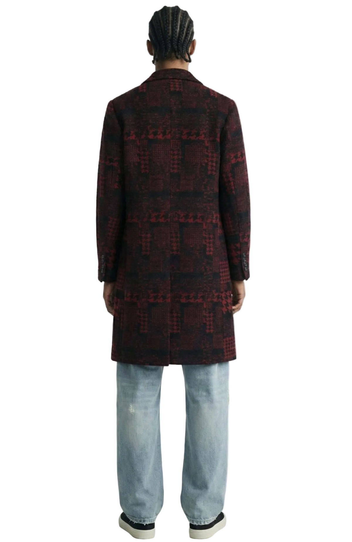 Person wearing a patterned coat and jeans on a white background