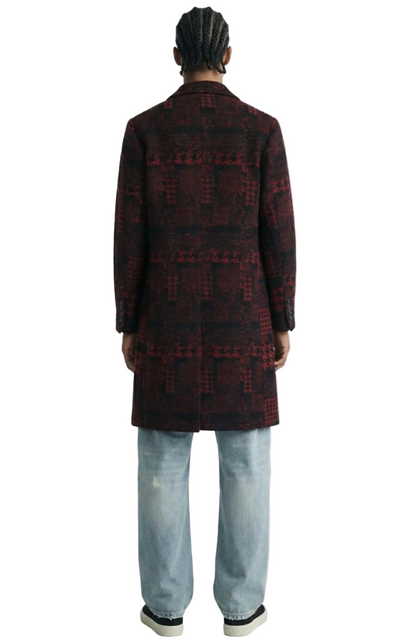 Person wearing a patterned coat and jeans on a white background
