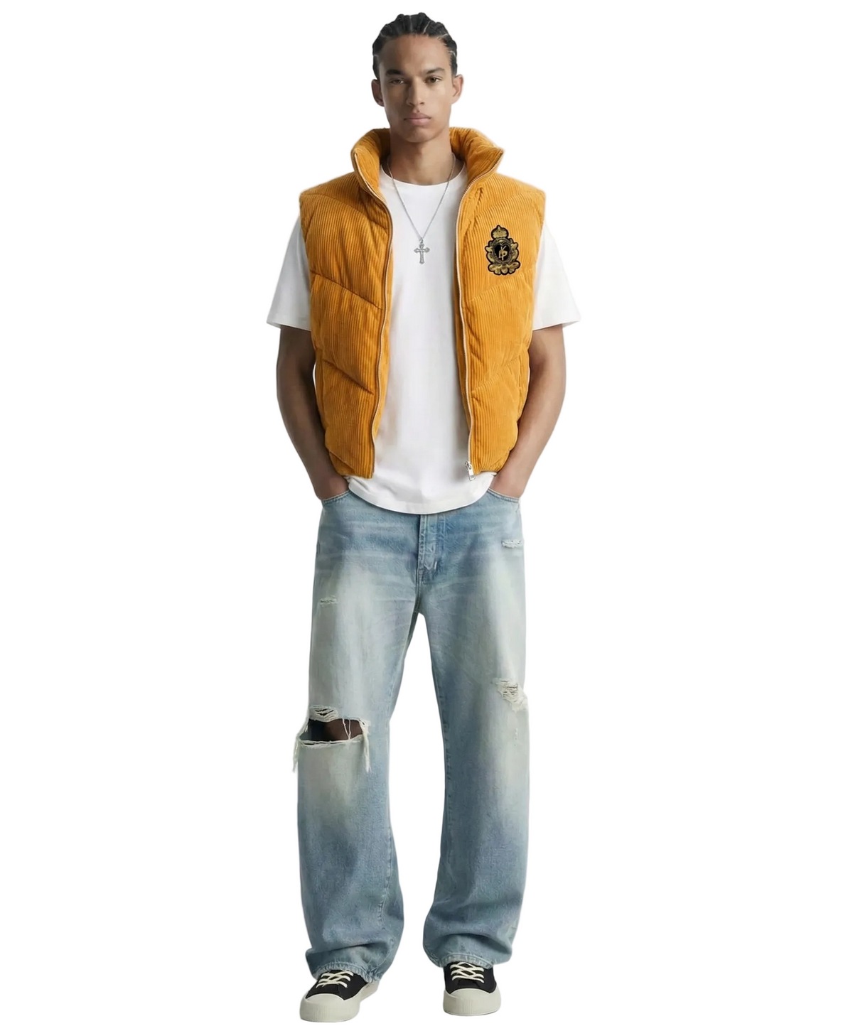 A male model wearing a mustard yellow puffer vest over a white t-shirt, paired with light-wash distressed jeans and black sneakers, shot against a solid white background.