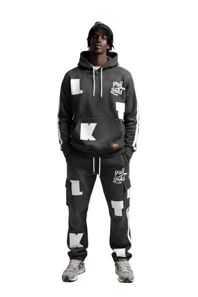 A man modeling a matching black hoodie and sweatpants set with white graphic lettering and logos, photographed against a solid white background.