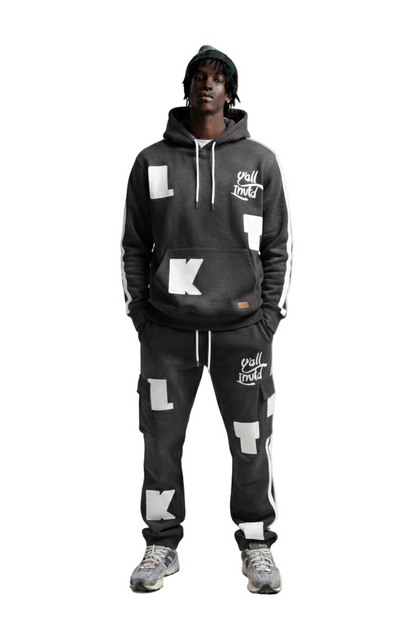 A man modeling a matching black hoodie and sweatpants set with white graphic lettering and logos, photographed against a solid white background.