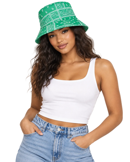 A woman wearing a green and white bandana print bucket hat, a white ribbed tank top, and light blue jeans, posing against a light gray studio background.