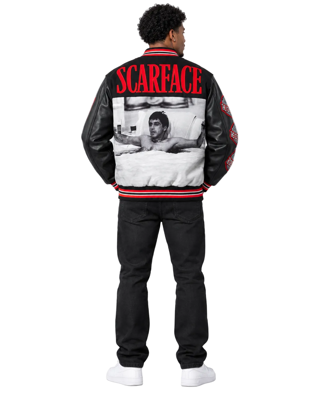 A man viewed from the back wearing a black leather-look Scarface varsity jacket with red and white trim, featuring a large black-and-white photo print and the word 'SCARFACE' in red across the upper back, paired with black pants and white sneakers on a white background.