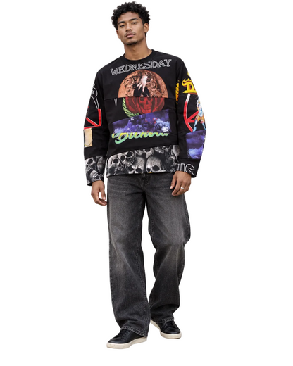 A man wearing a black graphic sweatshirt with colorful abstract prints, paired with dark gray jeans and black sneakers, standing outdoors against a concrete wall and metal door.
