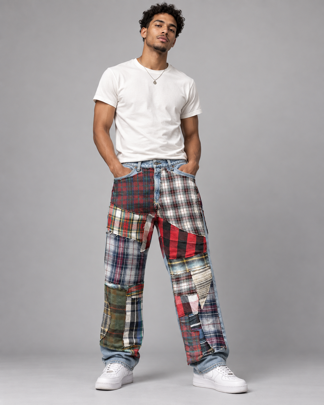 A man modeling a pair of patchwork plaid cargo pants with a white t-shirt and white sneakers, standing against a solid gray studio background.
