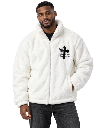 A man wearing a white sherpa fleece zip-up jacket with a black cross graphic on the chest, paired with dark gray jeans, against a plain white studio background.