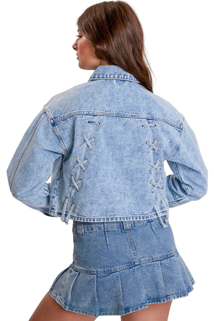 A model shown from the back wearing a light blue denim jacket and matching denim mini skirt. The jacket features decorative lace-up details on the back.