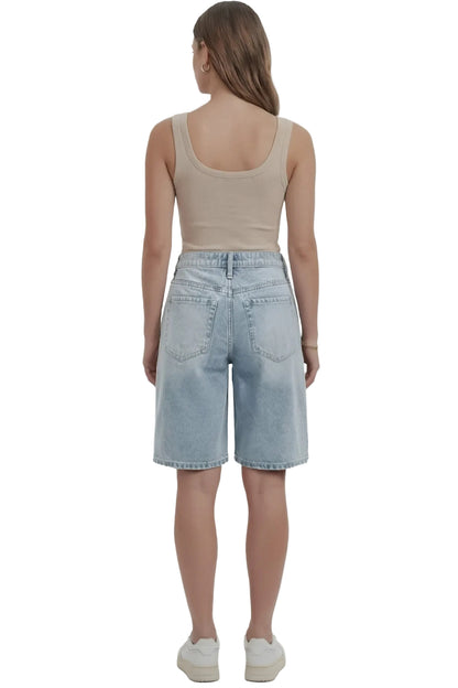 Person wearing a beige tank top and light blue denim shorts on a white background