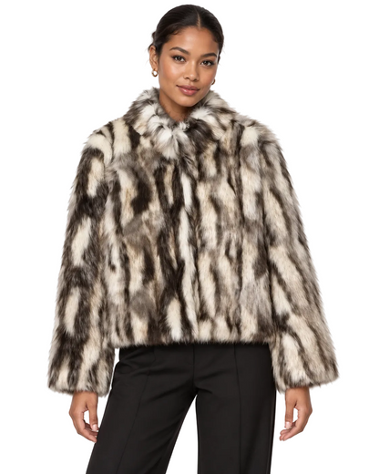 A model wearing a plush faux fur jacket with a brown, black, and beige animal-stripe pattern, paired with black trousers, against a plain white background.