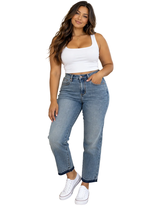 A woman modeling a pair of high-waisted, straight-leg blue jeans with a white crop top and white sneakers, standing in a modern living room setting.
