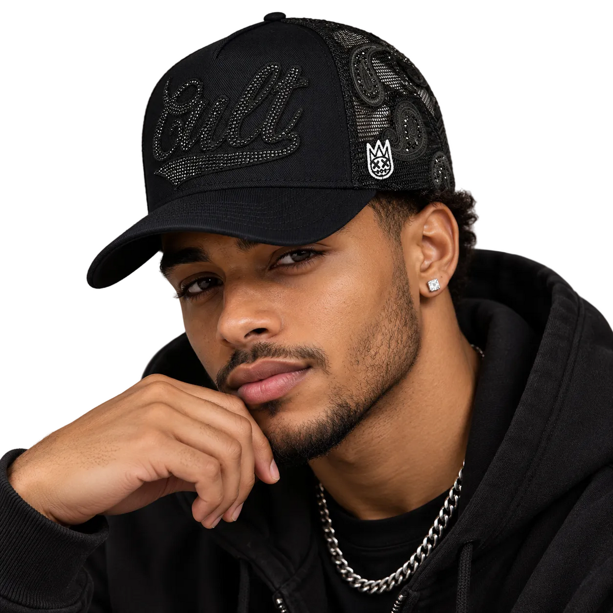 A man wearing a black baseball cap with rhinestone 'Cult' lettering on the front and a small white crest logo on the side, paired with a black hoodie and silver chain necklace against a neutral gray background.