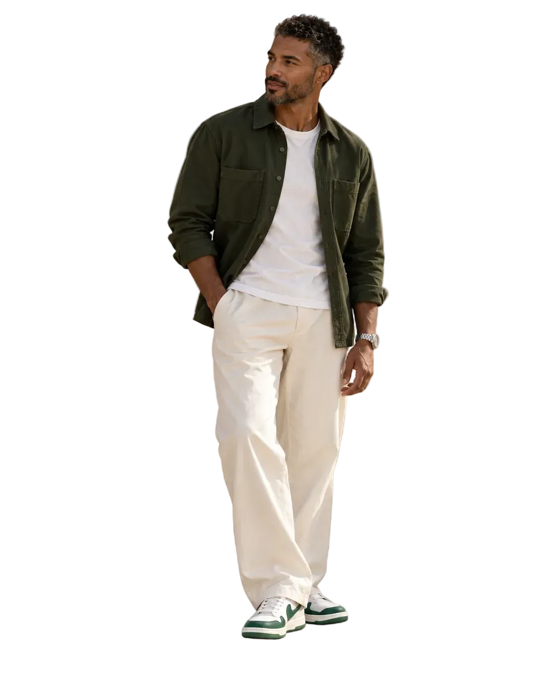 A man modeling a casual outfit consisting of an olive green overshirt, a white t-shirt, cream-colored trousers, and green and white sneakers, set against a solid gray background.