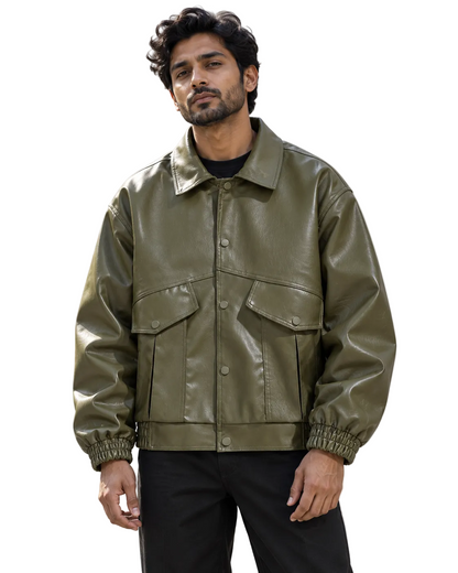 A man wearing an olive green faux leather jacket with snap-button front, flap chest pockets, and elasticized cuffs, standing outdoors against a light concrete building.