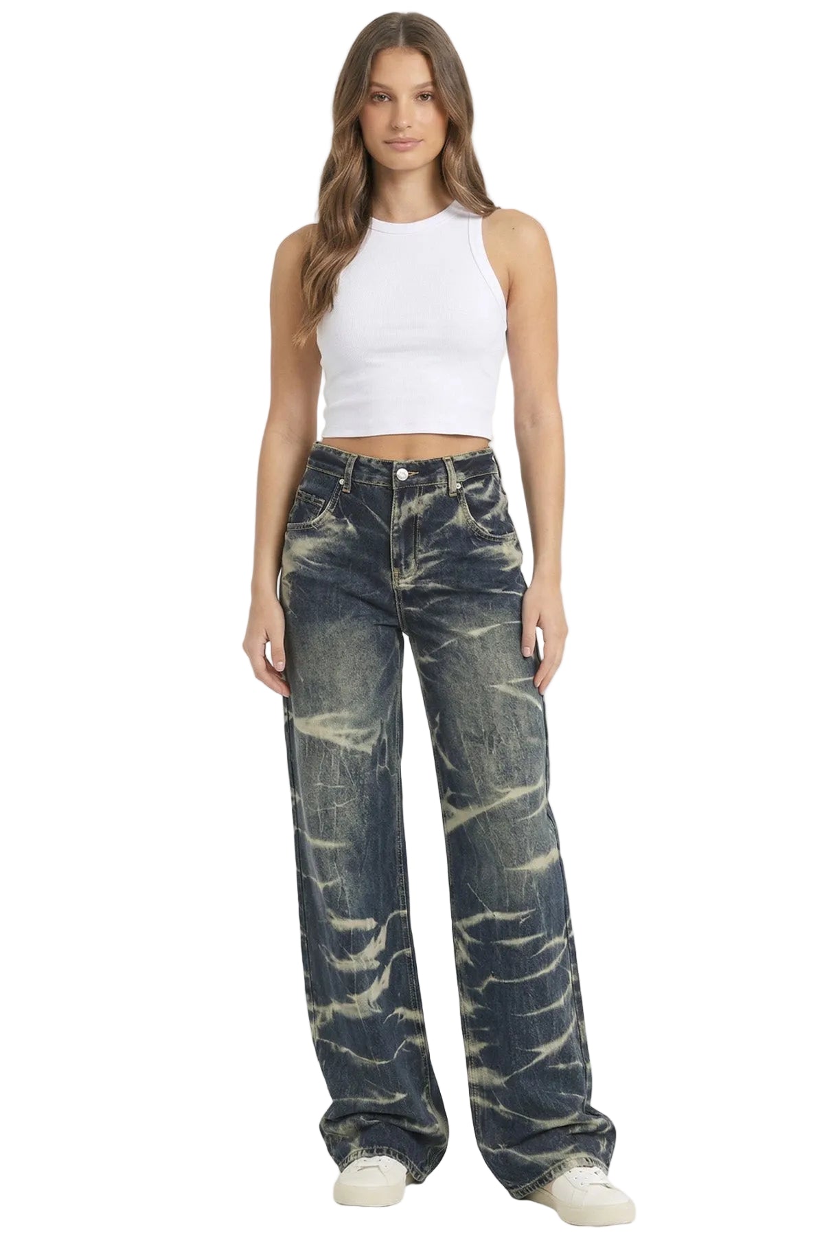 A woman modeling a pair of wide-leg, dark-wash jeans with a prominent bleach-blast or mineral-wash pattern in off-white, paired with a white sleeveless crop top and white sneakers, against a plain light gray studio background.