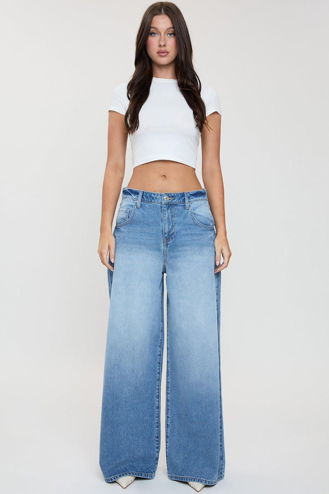 Woman wearing a white crop top and blue jeans on a plain background