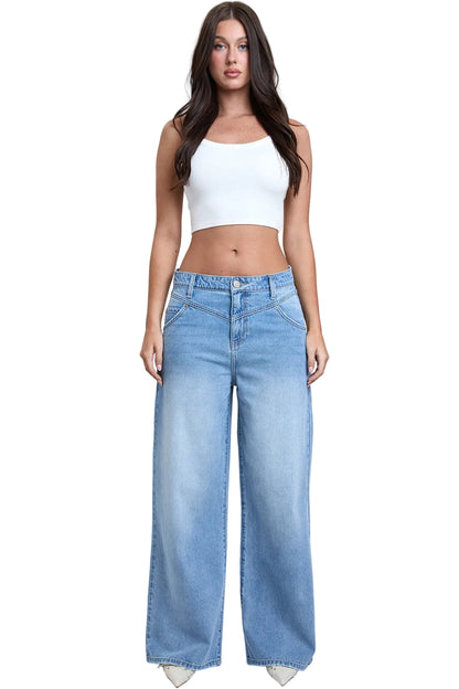 Woman wearing a white top and light blue wide-leg jeans on a plain background