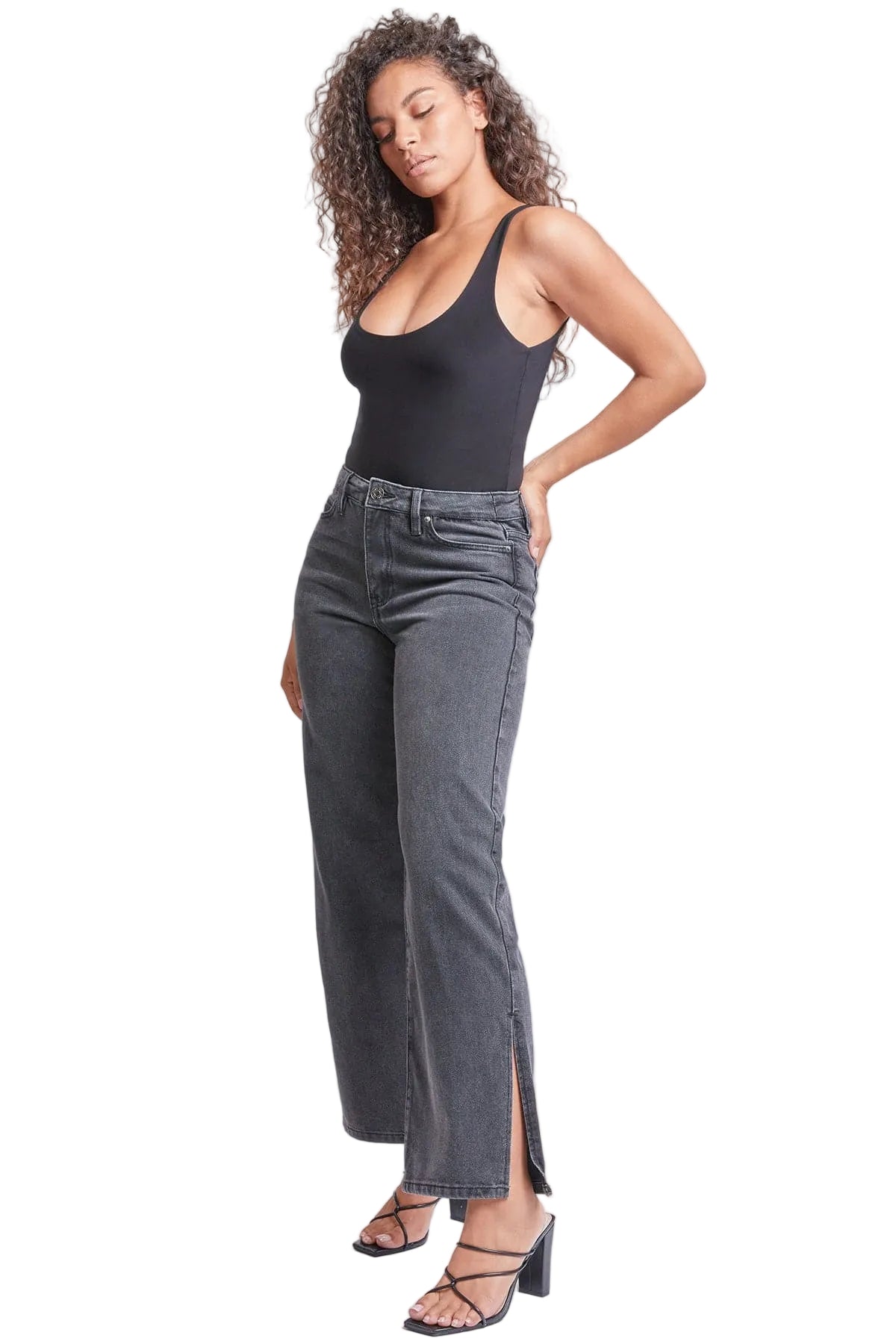 Woman wearing a black tank top and gray jeans with a slit on a white background