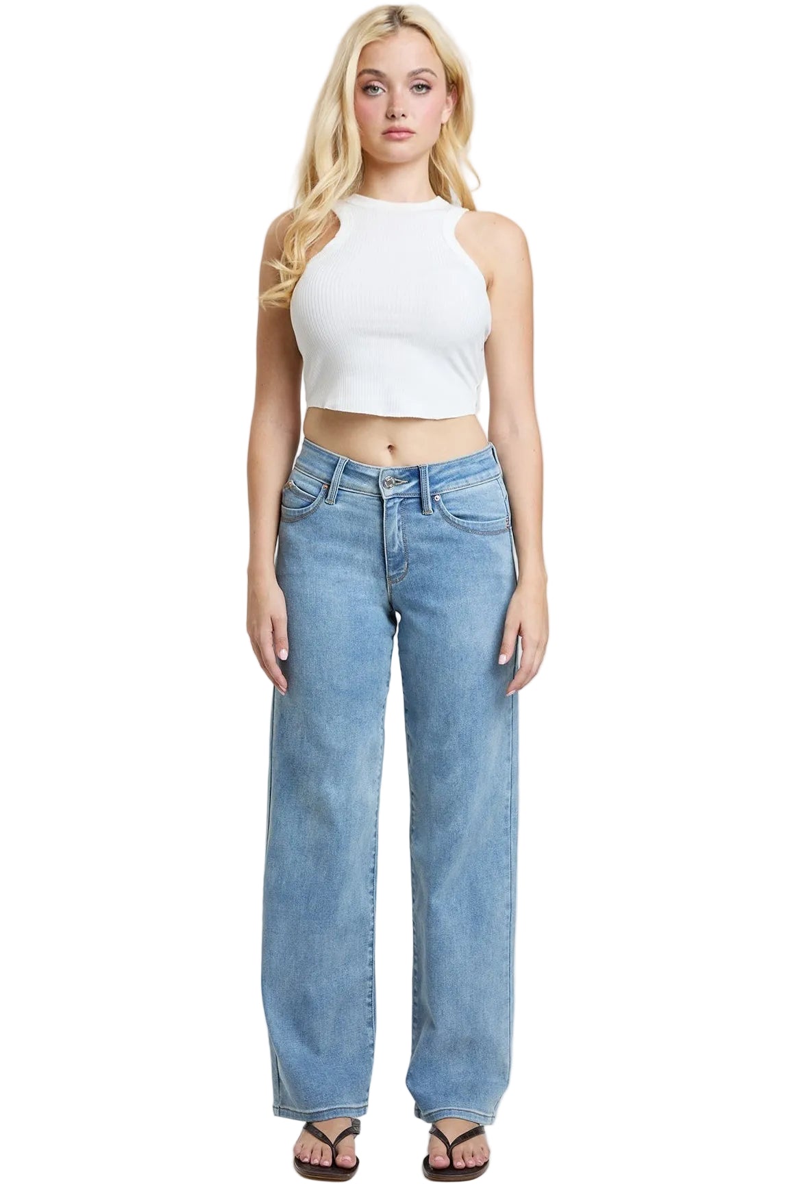 A blonde model stands against a light gray studio background wearing a white halter crop top and light-wash blue wide-leg jeans with black sandals.