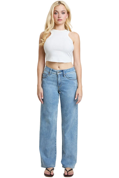 A blonde model stands against a light gray studio background wearing a white halter crop top and light-wash blue wide-leg jeans with black sandals.