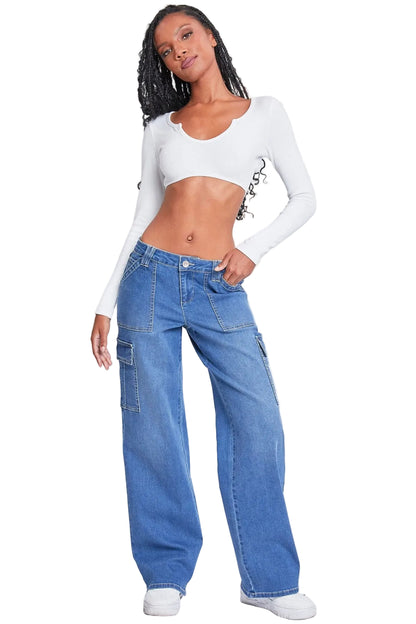 A model wearing a white long-sleeve crop top with black graphic text and blue wide-leg cargo jeans, paired with white sneakers, against a light gray studio background.