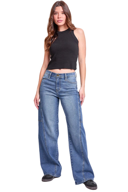 A woman modeling a black sleeveless crop top and wide-leg blue jeans against a plain light gray studio background.