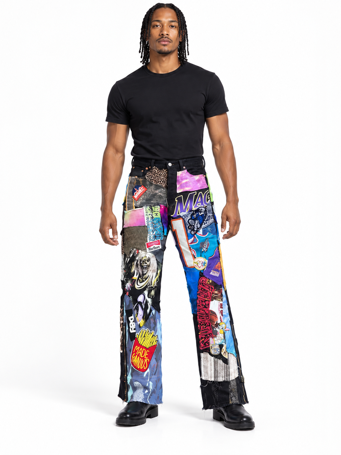 A man modeling a pair of wide-leg pants covered in a colorful collage print of comic book panels, posters, and graphic designs, paired with a black t-shirt and black shoes, on a white studio background.