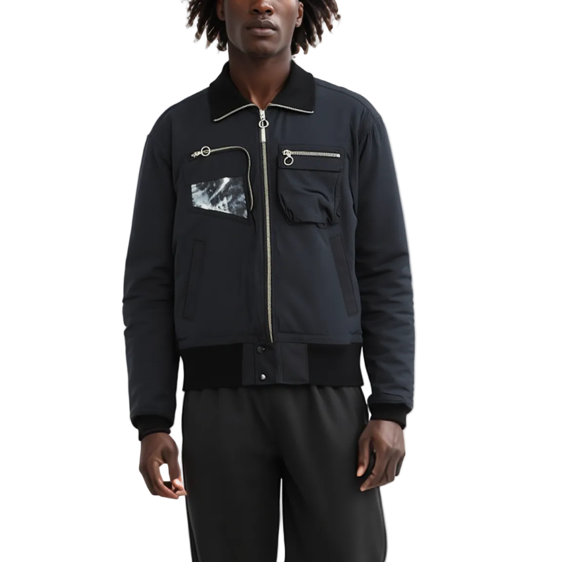 A man wearing a black bomber jacket with a silver zipper, a black-and-white marble patterned chest pocket, and black pants, photographed against a plain white studio background.