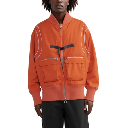 A model wearing a bright orange bomber jacket with white piping details, silver zippers, and a black belt detail at the chest, paired with black pants against a white studio background.