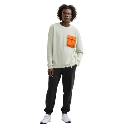 Man wearing a cream sweatshirt with an orange pocket and black pants on a white background