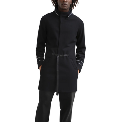 A model wearing a black mid-length coat with a high stand collar, a matching black belt, and white contrast piping on the collar, cuffs, and hem, paired with black trousers against a plain white background.