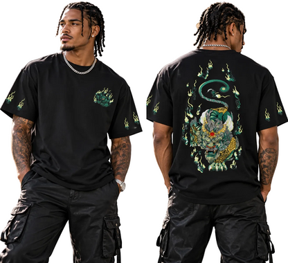 A man modeling a black short-sleeve graphic T-shirt in a split front and back view. The shirt has a green and gold snake-and-fish style graphic on the back and smaller green chest and sleeve graphics.