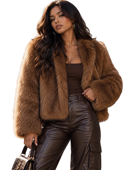 A woman stands outdoors wearing a voluminous brown faux-fur jacket over a dark brown top and shiny dark brown pants, holding a small black handbag.