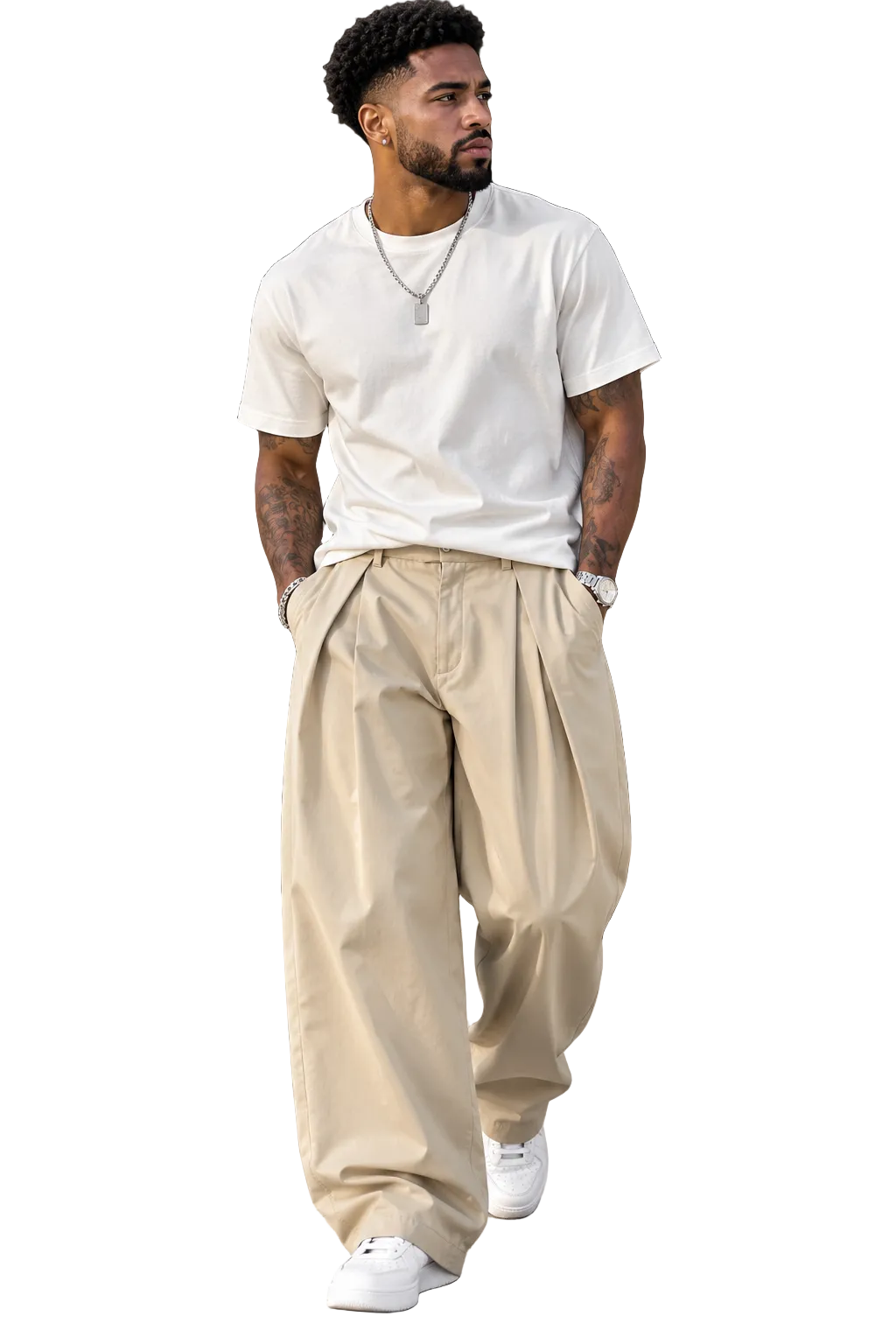 A man walking outdoors wearing a white crew-neck t-shirt, loose beige pleated trousers, and white sneakers.
