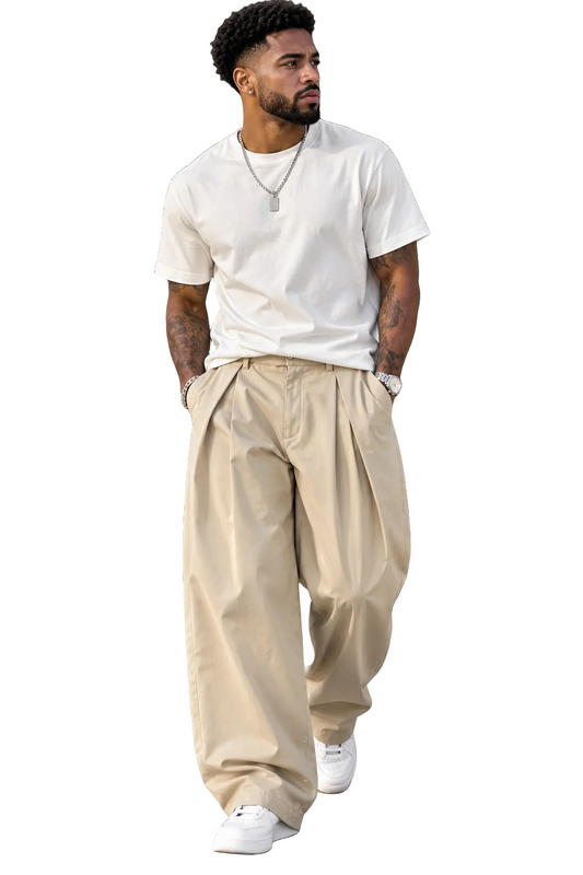 A man walking outdoors wearing a white crew-neck t-shirt, loose beige pleated trousers, and white sneakers.
