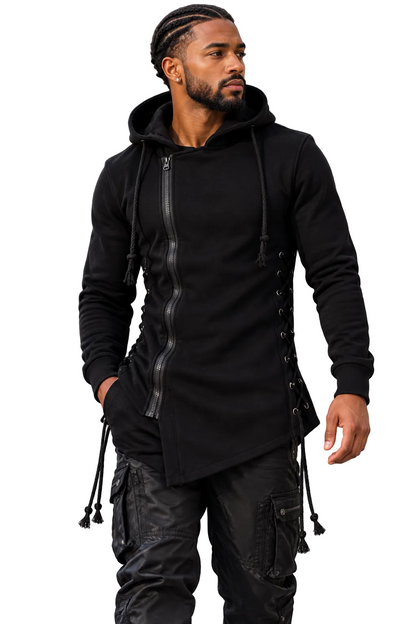 A man wearing a black hooded long-sleeve top with a front zipper, side laces, and drawstrings, paired with black cargo pants, standing outdoors against a gray building background.