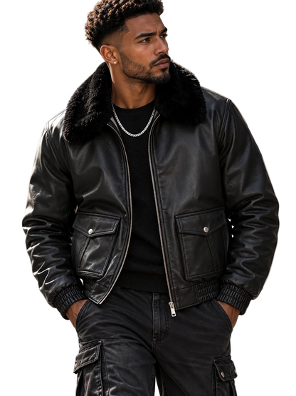 A man wearing a black leather bomber jacket with a black faux-fur collar, styled with a black t-shirt, silver chain necklace, and black cargo pants, standing in an urban setting.