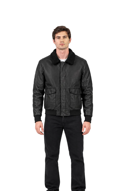 A man wearing a black leather bomber jacket with a black corduroy collar, black ribbed cuffs and hem, paired with black jeans, shot against a solid white background.