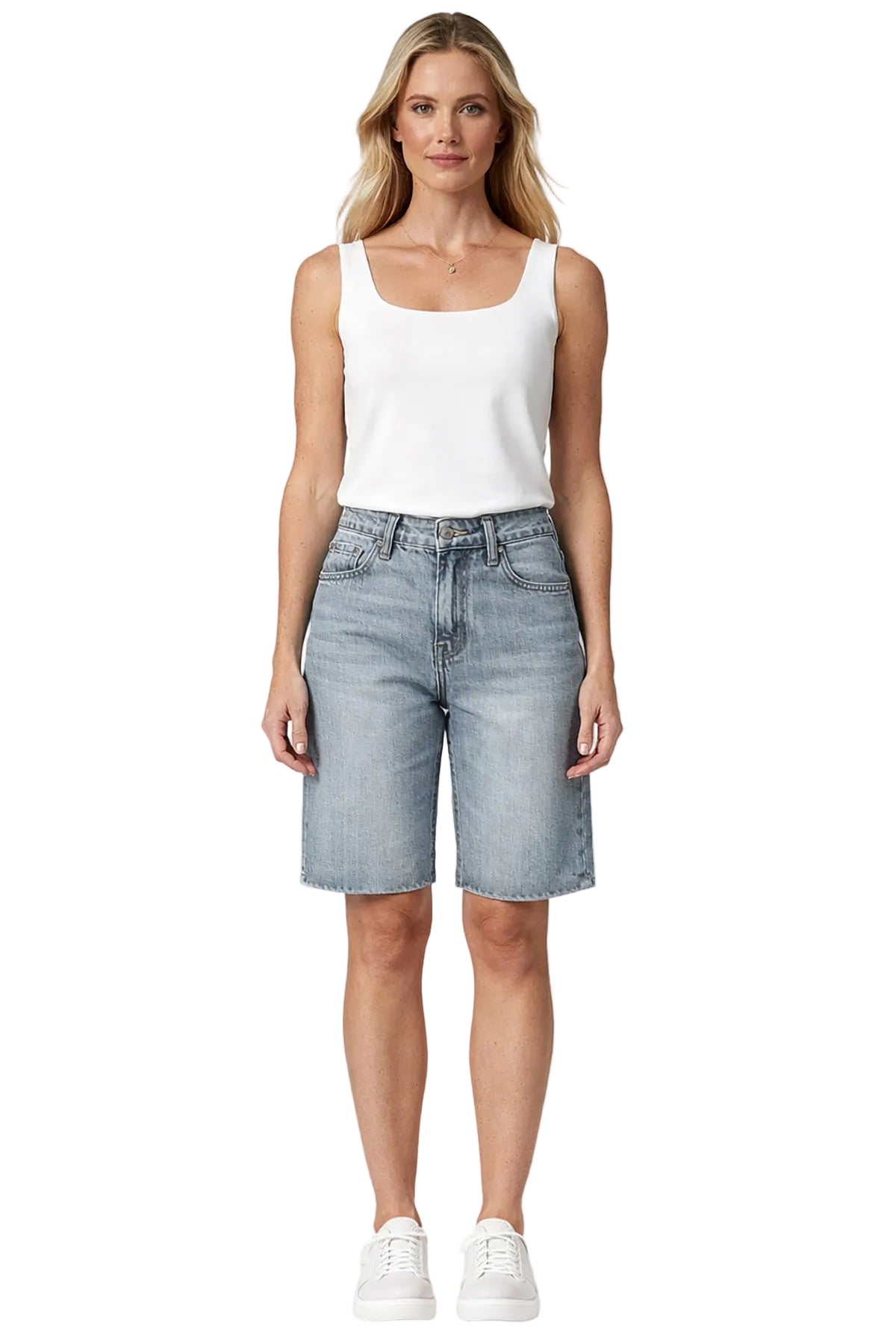 A woman modeling a white sleeveless tank top and light-wash denim shorts against a plain light gray studio background.