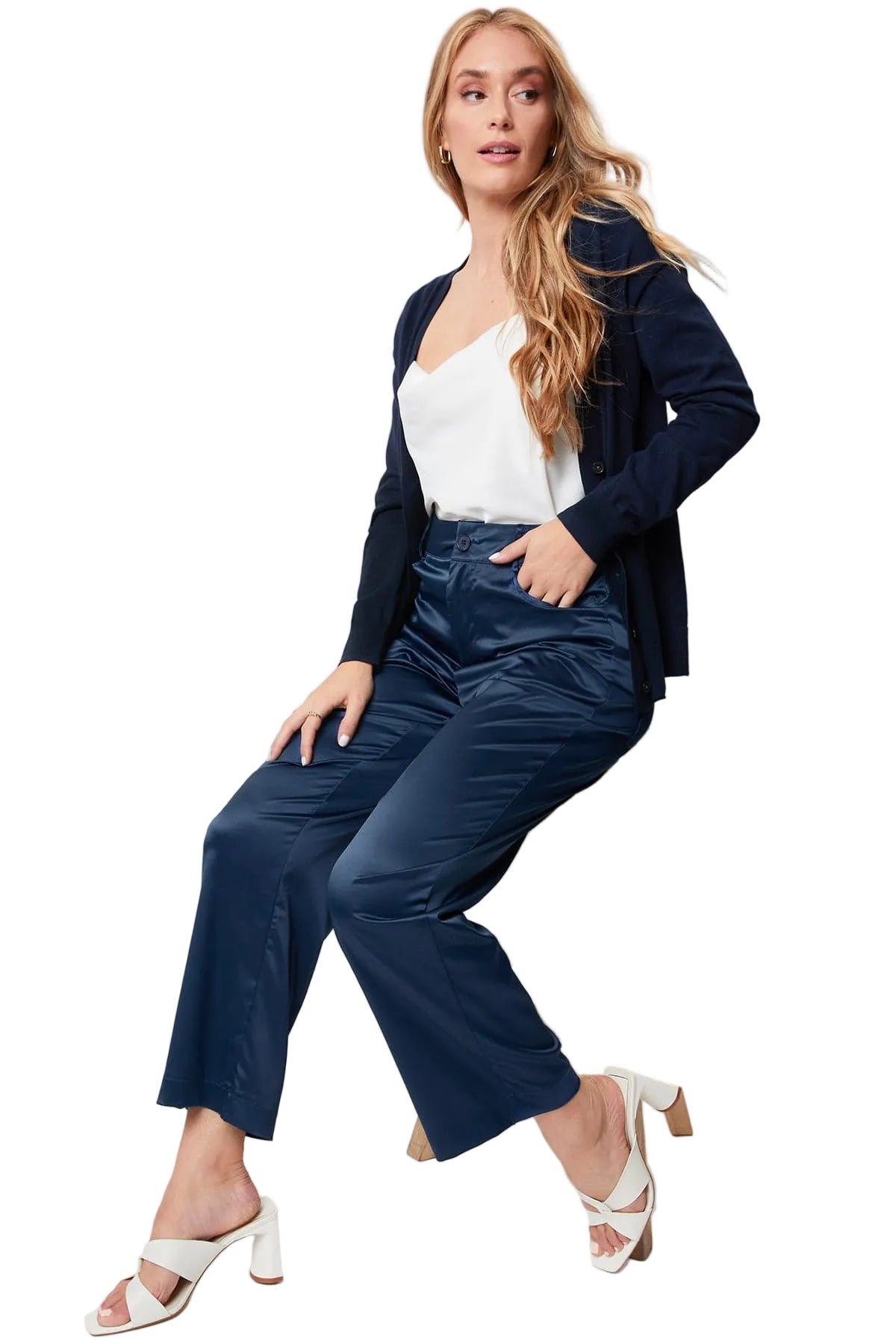 Woman wearing a navy blazer and pants sitting on a stool against a white background