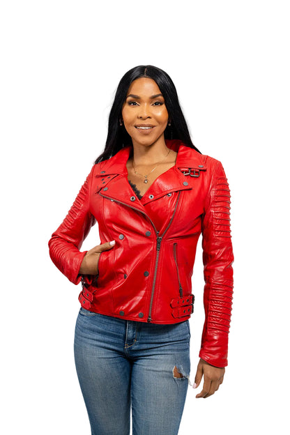 A woman modeling a bright red faux leather motorcycle jacket with silver zippers and snap buttons, paired with blue jeans, against a light gray studio background.
