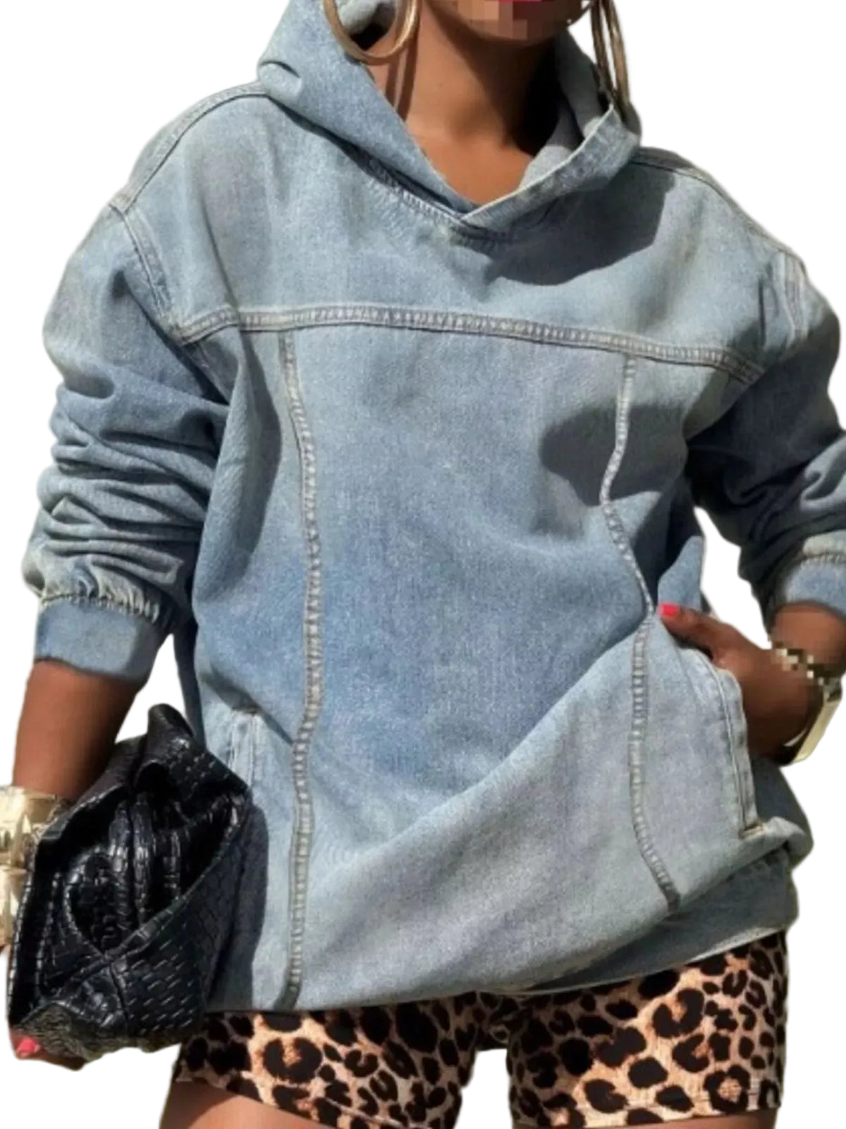 A person wearing an oversized light-wash blue denim hoodie with front seam detailing and side pockets, paired with leopard-print shorts and holding a black textured clutch.