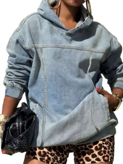 A person wearing an oversized light-wash blue denim hoodie with front seam detailing and side pockets, paired with leopard-print shorts and holding a black textured clutch.
